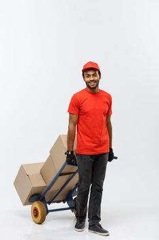 Delivery Concept - Portrait of Handsome African American delivery man or courier pushing hand truck with stack of boxes. Isolated on Grey studio Background. Copy Space