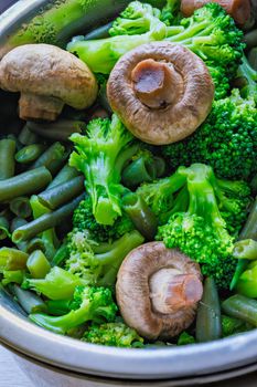 boiled green vegetables - broccoli, green beans and champignon mushrooms in stainless steel colander - full-frame closeup