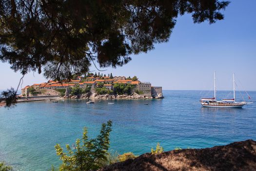 Famous architectural monument of the island resort of St. Stephen St. Stephen in the Adriatic Sea, Montenegro. The concept of vacation at sea, boat in the sea. Photo through the trees