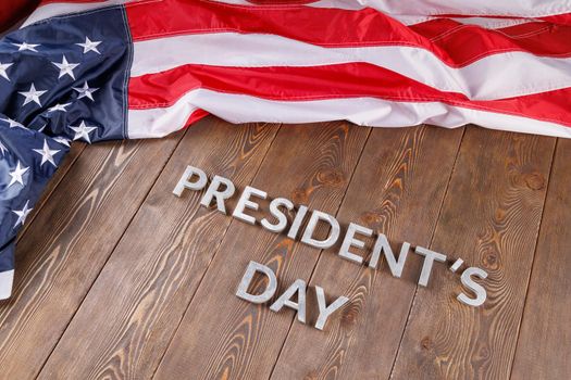 words presitdents day laid with silver metal letters on wooden surface near crumpled US flag