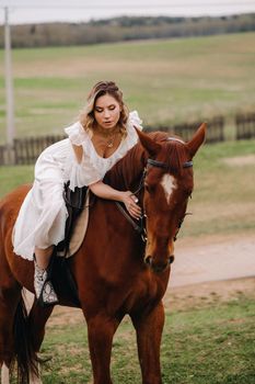 A woman in a white sundress riding a horse in a field.