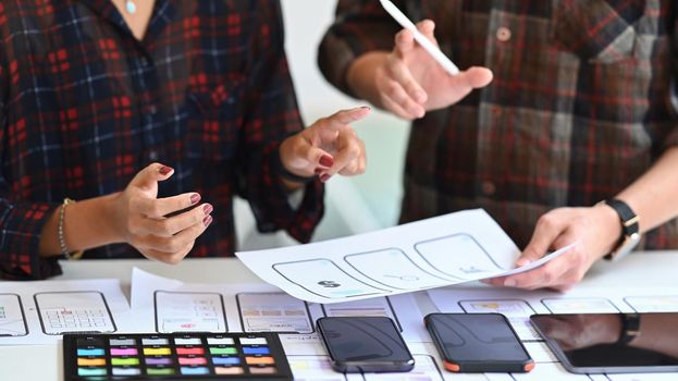 Cropped shot of designers creating mobile application prototype at office desk.