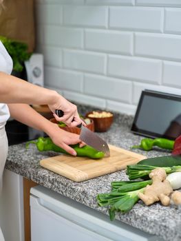 female cook chopping vegetables on a wooden plank, tablet leaning against the wall to see the recipe, vertical image