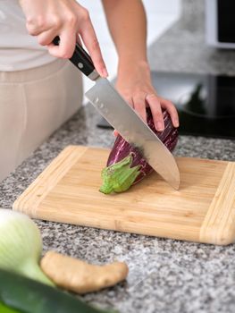 person cutting an eggplant with a knife on a wooden plank, close-up vertical view