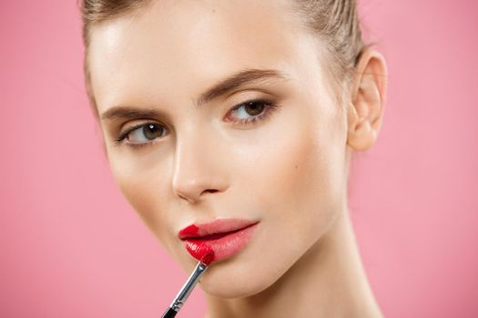 Beauty Concept - Woman applying red lipstick with pink studio background. Beautiful girl makes makeup