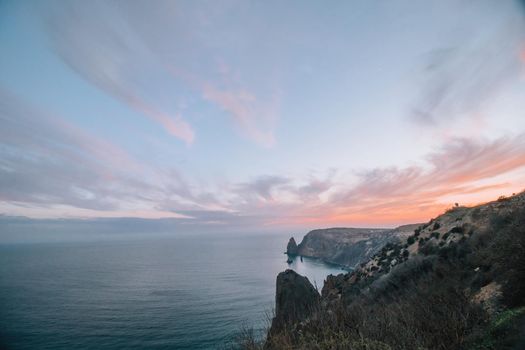 A red burning sunset with the silhouette of a cliff over the sea. Abstract nature summer or spring ocean sea background. Small waves on golden warm water surface with bokeh lights from sun.