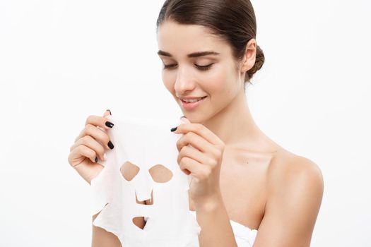 Beauty Skin Care Concept - Beautiful Caucasian Woman applying paper sheet mask on her face white background