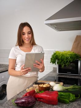 cook looking for a vegan food recipe on her tablet, standing in front of the worktop, vertical portrait