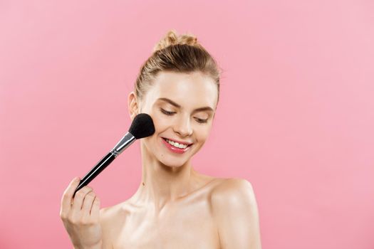 Beauty Concept - Closeup Beautiful caucasian woman applying makeup with Cosmetic Powder Brush. Perfect Skin. Isolated on pink background and copy space