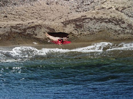 Young sensual blonde woman sitting on the rock near water at sea and enjoys the sea waves on background of two volcanic rocks, like in Iceland. Dreams holidays and weekend vacation in summer time
