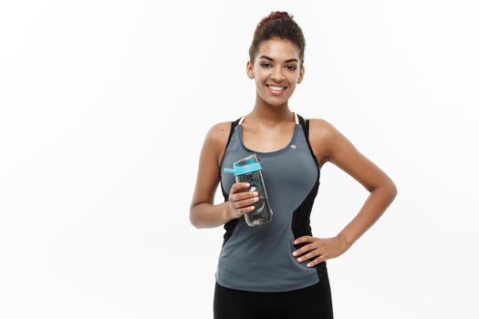 Healthy and Fitness concept - beautiful African American girl in sport clothes holding water bottle after workout. Isolated on white studio background.