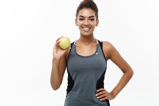 Healthy and Fitness concept - Beautiful American African lady in grey fitness clothes holding green apple. Isolated on white background