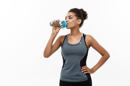 Healthy and Fitness concept - beautiful African American girl in sport clothes drinking water after workout. Isolated on white studio background.