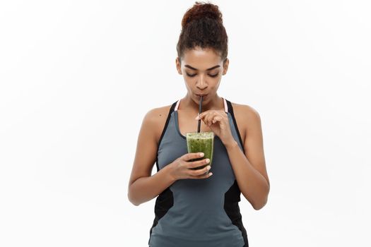 Healthy and Fitness concept - Beautiful American African lady in fitness clothing drinking healthy vegetable drink. Isolated on white background