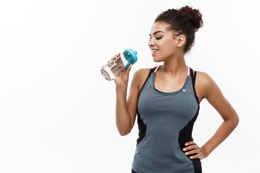 Healthy and Fitness concept - beautiful African American girl in sport clothes drinking water after workout. Isolated on white studio background.