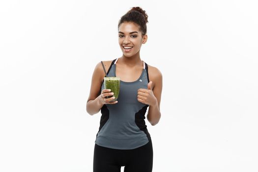 Healthy and Fitness concept - Beautiful American African lady in fitness clothing drinking healthy vegetable drink. Isolated on white background