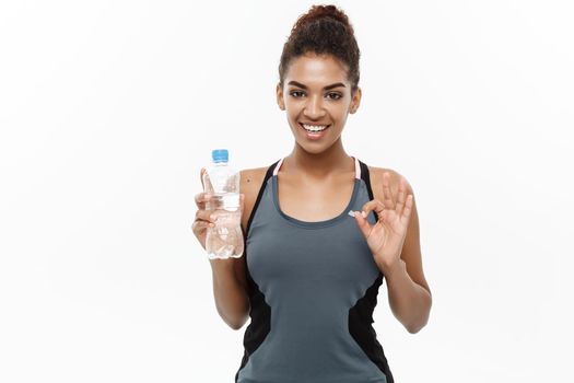 Healthy and Fitness concept - beautiful African American girl in sport clothes holding plastic water bottle after workout. Isolated on white studio background.