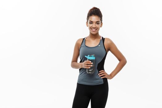 Healthy and Fitness concept - beautiful African American girl in sport clothes holding water bottle after workout. Isolated on white studio background.