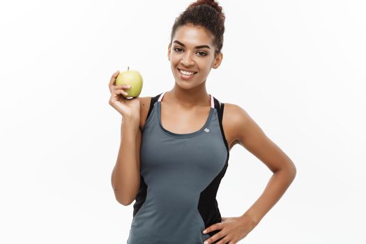 Healthy and Fitness concept - Beautiful American African lady in grey fitness clothes holding green apple. Isolated on white background