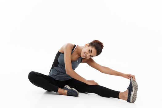 Sport, training, lifestyle and Fitness concept - portrait of beautiful happy African American woman stretching leg while sitting. Isolated on white studio background