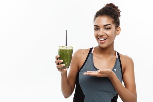 Healthy and Fitness concept - Beautiful American African lady in fitness clothing drinking healthy vegetable drink. Isolated on white background