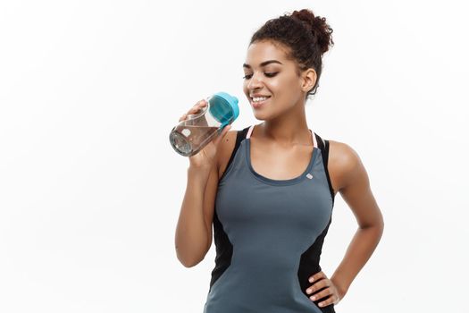 Healthy and Fitness concept - beautiful African American girl in sport clothes drinking water after workout. Isolated on white studio background.