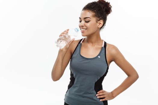 Healthy and Fitness concept - beautiful African American girl in sport clothes drinking water by plastic bottle after workout. Isolated on white studio background.