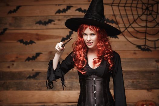 Halloween witch concept - Happy Halloween red hair Witch holding posing with magic wand over old wooden studio background