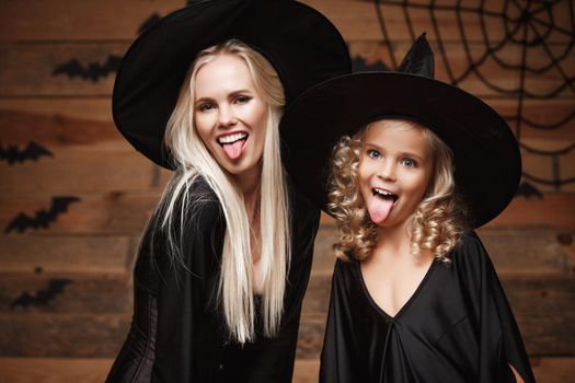 Halloween Concept - Closeup beautiful caucasian mother and her daughter in witch costumes celebrating Halloween posing with curved pumpkins over bats