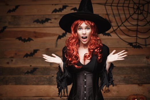 Halloween witch concept - Happy Halloween red hair Witch holding posing with shocked face over old wooden studio background