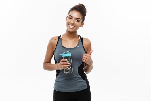 Healthy and Fitness concept - beautiful African American girl in sport clothes holding water bottle after workout. Isolated on white studio background.