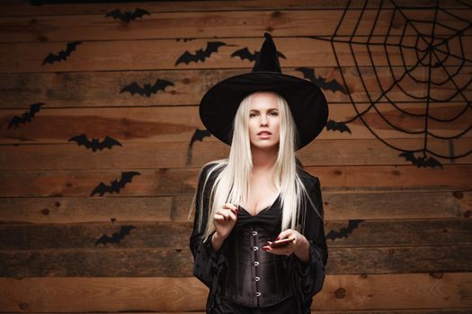 Halloween witch concept - Happy Halloween Sexy Witch holding posing with smartphone over old wooden studio background