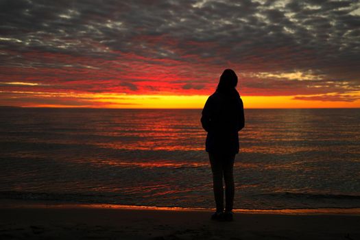 Silhouette of Young Adolescent Girl Looks up in Awe, Wonder, and Admiration at a Magnificent Sunset Sky while Standing on Wasaga Beach with Georgian Bay in background. Rear View. High quality photo