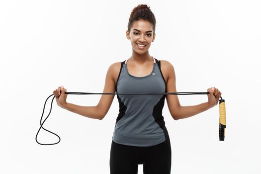 Sport, training, lifestyle and Fitness concept - portrait of beautiful happy African American woman exercising with jumping rope. Isolated on white studio background