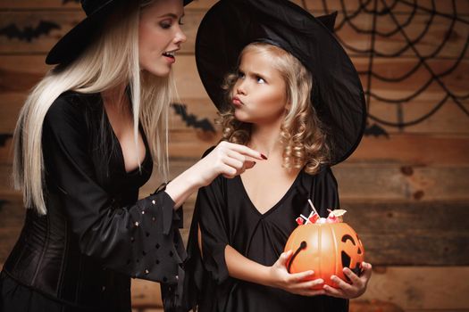 Halloween Concept: beautiful caucasian mother playing with her little daugther enjoy with Halloween candy and sweet over bats and spider web on Wooden studio background