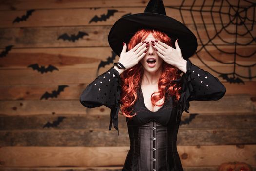 Halloween witch concept - Happy Halloween red hair Witch holding hands closing eyes posing over old wooden studio background