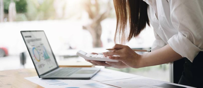 Asian female accountant or banker making calculations. Savings, finances and economy concept through a laptop..