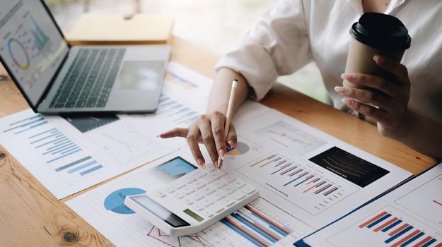 Close up Business woman using calculator and laptop for do math finance on wooden desk in office and business working background, tax, accounting, statistics and analytic research concept.