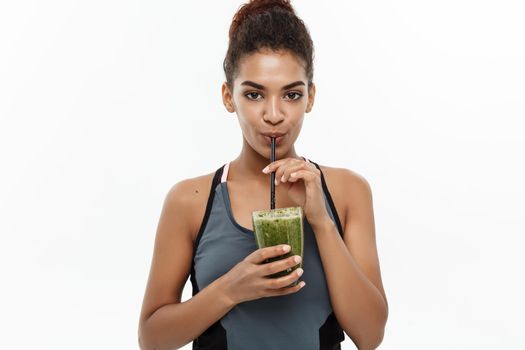 Healthy and Fitness concept - Beautiful American African lady in fitness clothing drinking healthy vegetable drink. Isolated on white background