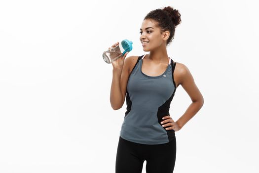 Healthy and Fitness concept - beautiful African American girl in sport clothes drinking water after workout. Isolated on white studio background.