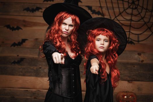 Halloween Concept - Beautiful caucasian mother and her daughter with long red hair in witch costumes with angry fussy facial expression and pointing finger to camera