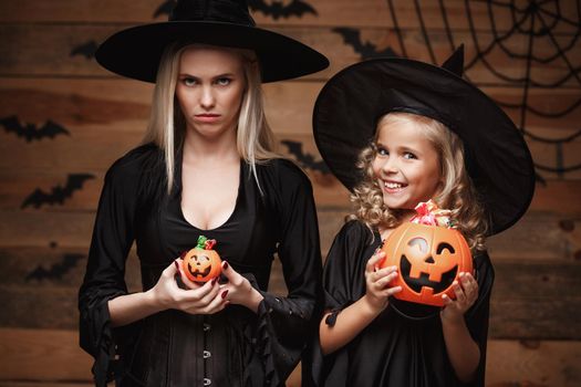 Halloween Concept: beautiful caucasian mother with disappointed feeling with happy little daugther enjoy with Halloween candy and sweet over bats and spider web on Wooden studio background