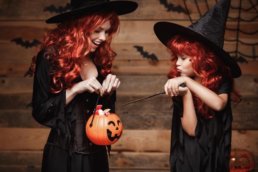 Halloween Concept - Beautiful caucasian mother and her daughter with long red hair in witch costumes with Halloween candy and magic wand