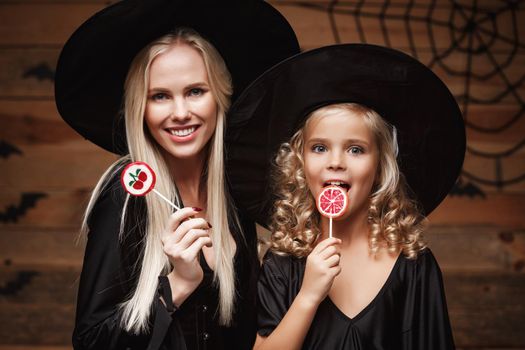 Halloween Concept: beautiful caucasian mother and her daughter in witch costumes celebrating Halloween with Halloween candy and sweet over bats and spider web on Wooden studio background