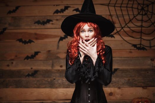 Halloween witch concept - Happy Halloween red hair Witch holding posing with shocked face over old wooden studio background