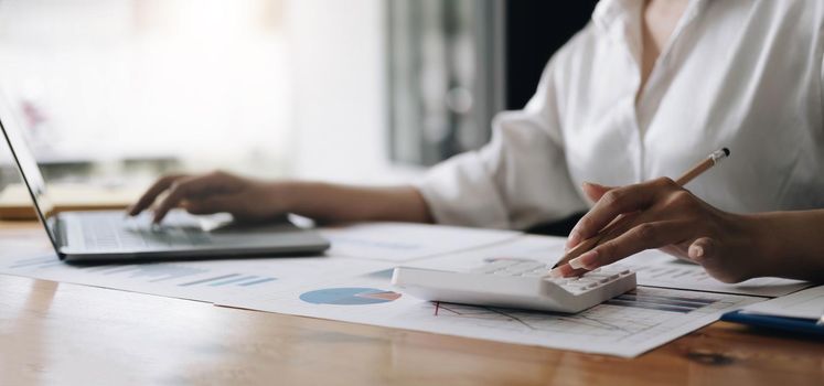 Close up Business woman using calculator and laptop for do math finance on wooden desk in office and business working background, tax, accounting, statistics and analytic research concept.