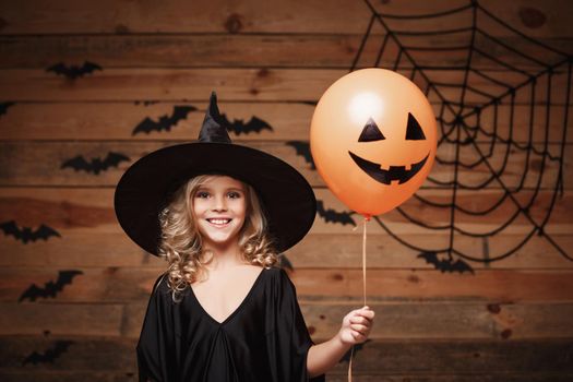 Halloween Witch concept - little caucasian witch child enjoy with halloween balloon. over bat and spider web background