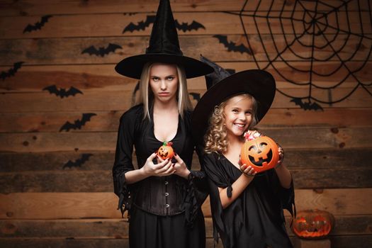 Halloween Concept: beautiful caucasian mother with disappointed feeling with happy little daugther enjoy with Halloween candy and sweet over bats and spider web on Wooden studio background