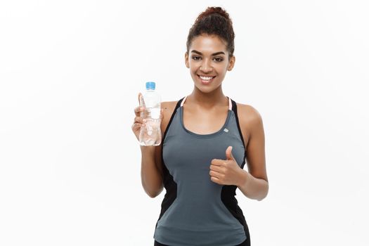 Healthy and Fitness concept - beautiful African American girl in sport clothes holding plastic water bottle after workout. Isolated on white studio background.