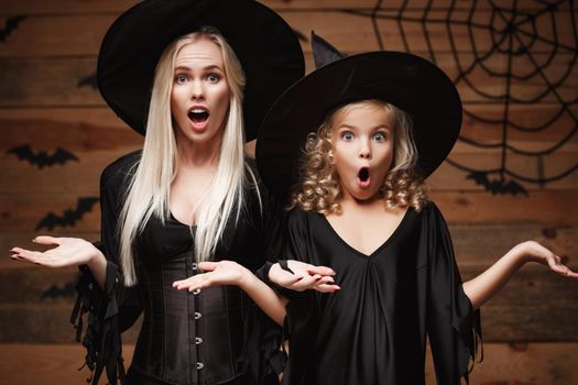 Halloween Concept - Closeup beautiful caucasian mother and her daughter in witch costumes celebrating Halloween posing with curved pumpkins over bats